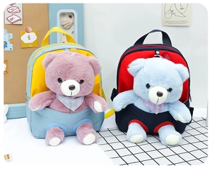 Detail of two colorful kids backpacks featuring detachable plush bear toys in front pockets