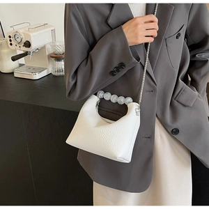 Detailed shot of white textured leather pearl handle bag with silver chain strap on model