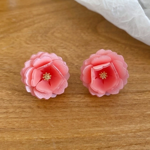 Gros plan de boucles d'oreilles fleurs en résine rose avec étamines dorées sur bois