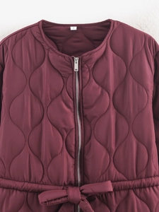 Close-up of wine red quilted jacket featuring zipper and stylish waist bow-tie