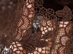 Dettaglio macro in pizzo marrone scuro con ricamo floreale e trama semitrasparente