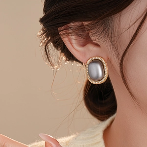 Close-up of gold round earrings with grey center and zircon halo on female model