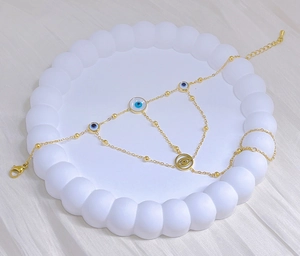 Detail of golden Evil Eye hand chain bracelet with blue charms on a white tray