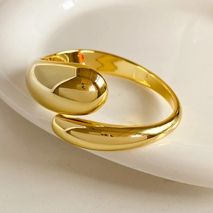 Macro detail of a polished gold cross-over open bangle resting on a ceramic surface