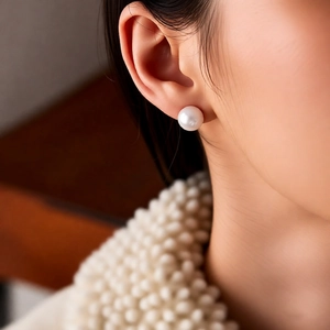 Detailed view of elegant white round pearl stud earrings worn by a female model