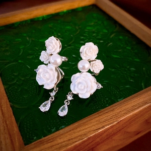 Close-up of elegant white rose earrings with hanging pearls and teardrop crystals