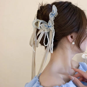Détail d'une pince à cheveux papillon brodé avec pompons en perles et rubans en satin