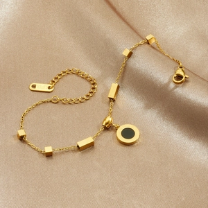 Golden stainless steel chain bracelet with black roman coin pendant on silk background