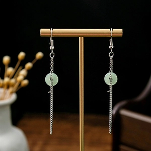 Detail of silver long tassel earrings with light green jade-like beads on a display stand