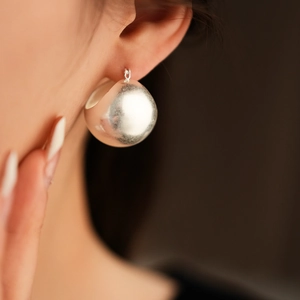 Close-up of minimalist silver spherical hoop earrings on model with matte finish