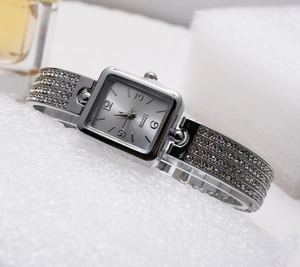 Close-up of square quartz watch featuring a sparkling rhinestone bracelet and silver dial