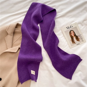 Flat lay of a purple knit scarf with a beige coat and fashion magazine for winter vibes