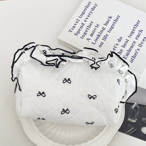 Close-up of white quilted makeup bag with bow embroidery and ruffled edge details