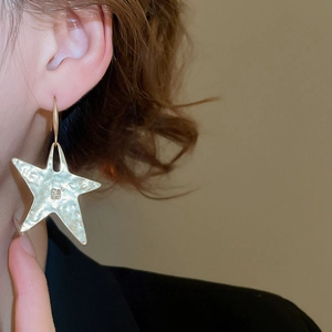Detailed close-up of gold star earrings with hammered texture on a fashion model