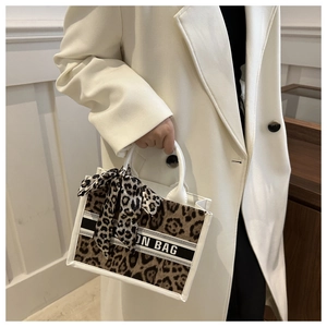 Close-up of leopard print tote bag with black strap detail and decorative silk scarf handle
