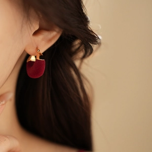 Close-up of C-shaped gold-plated earrings with burgundy flocking velvet detail