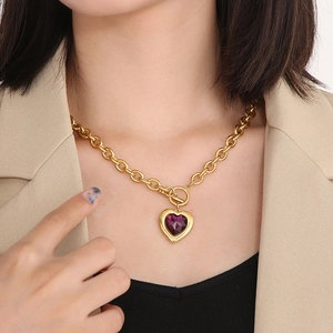 Détail de la chaîne dorée à boucle OT et pendentif cœur en cristal violet sur le cou