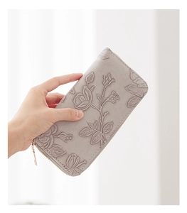 Close-up of grey long wallet with rose floral embossing and gold metal zipper detail