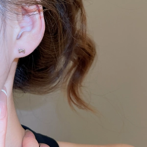 Close-up of 18k gold plated bow stud earring with zircons worn on ear lobe