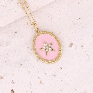 Close-up of golden star necklace with pink enamel oval pendant and zircon stone