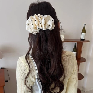 Close-up of a cream polka dot fabric hair tie styled on a model in a warm home setting