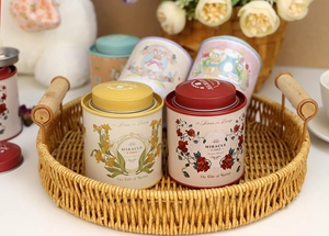 Close-up of vintage floral tin cans in a woven tray with tea time atmosphere