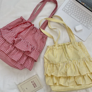 Flat lay of plaid canvas tote bags with ruffle trim, drawstring closure and laptop