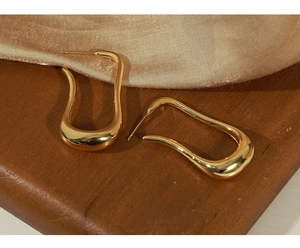Detailed view of polished golden irregular U-shaped copper earrings on a fabric texture