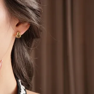 Elegant 18k gold plated gourd stud earrings worn by model on a textured brown background