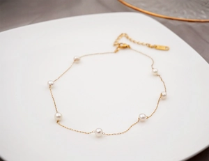 Close-up of golden stainless steel necklace with fresh water pearls on a white plate