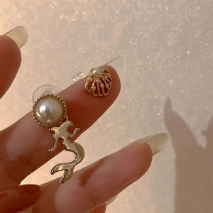 Macro view of gold asymmetric mermaid and shell earrings with inlaid pearls