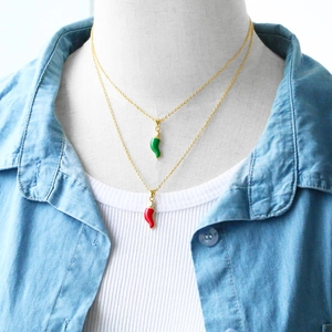 Detail of red and green chili pepper enamel pendant necklaces worn with a denim shirt