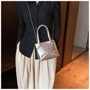 Close-up of a silver handbag featuring bow decorations and a metallic chain strap
