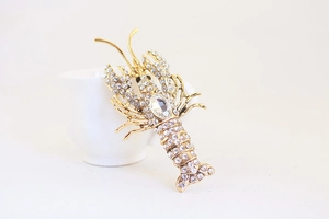 Detailed view of a gold-plated lobster brooch with crystal rhinestones on a white cup