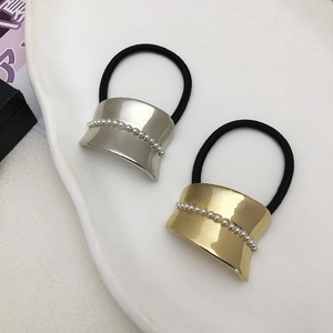 Elegant gold and silver hair ties with pearl-rimmed metal plates on white ceramic