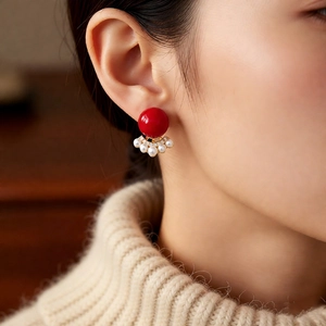 Close-up of elegant gold stud earring with red bead and fan-shaped pearl accents