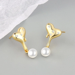 Macro shot of gold heart-shaped stud earrings with zircon inlay and hanging white pearl