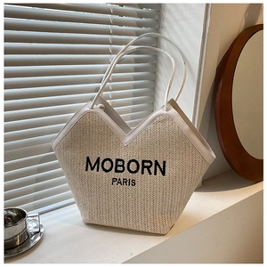 Detail of woven straw tote bag featuring black MOBORN PARIS embroidery and white leather trim