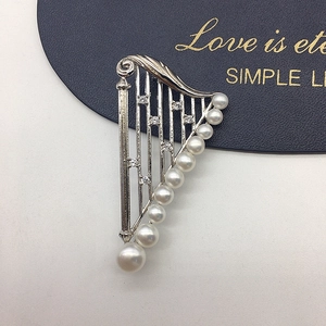 Macro shot of silver harp brooch featuring gradient freshwater pearls and micro-pave crystals