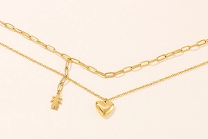 Detail of a double-layered gold necklace with paperclip chain and heart and girl charms
