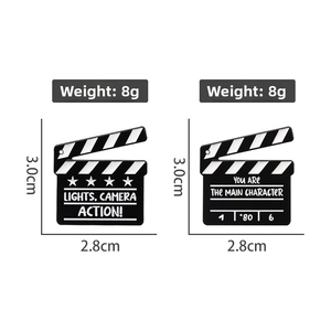 Detail showing two film clapperboard enamel pins with size and weight dimensions