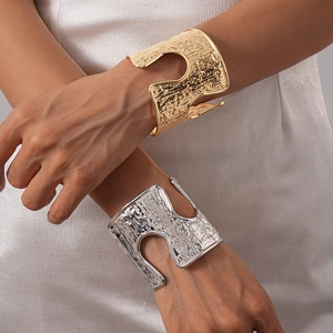 Detailed view of wide metallic cuffs with hammered texture and wavy cutout patterns