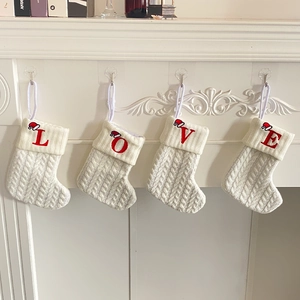 Set of four white knitted Christmas stockings with LOVE embroidery hanging on mantel