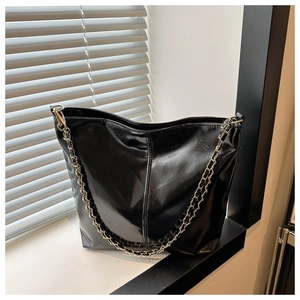 Detail of black glossy tote bag featuring a gold chain strap and elegant stitching