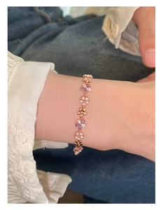 Detail of rose gold bracelet with white pearls and purple zircon flowers on model's wrist