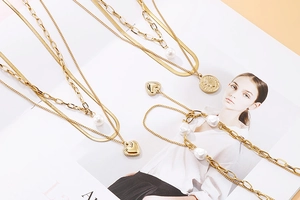 Mise à plat de colliers dorés superposés avec cœur, perle baroque et détails de pièces