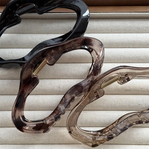 Three elegant hair claws in black and tortoiseshell finishes on a textured beige surface