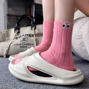 Close-up of pink ribbed mid-calf socks featuring cute cartoon eye embroidery with beige slippers