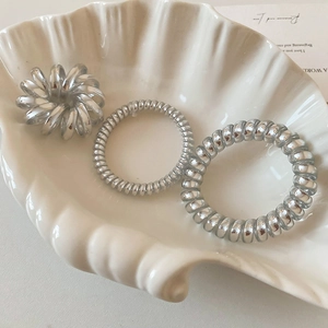 Three metallic silver spiral hair ties displayed on a decorative white shell tray