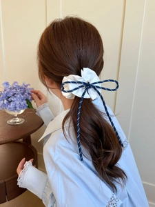 Close-up of white pleated scrunchie with blue dotted bow hair tie worn on a model